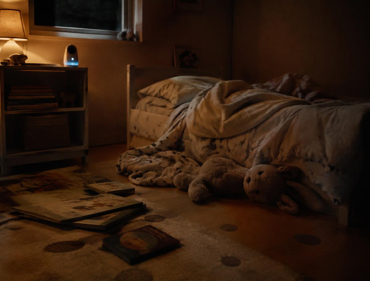 A child's bedroom after bedtime: crumpled blanket, worn stuffed animals, books on the floor.