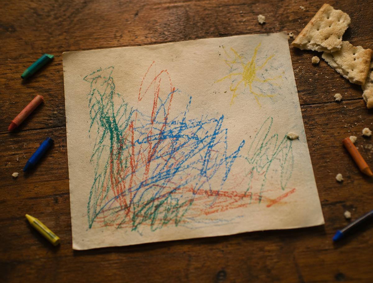 A child's crayon drawing on paper with broken crayons and cracker crumbs.