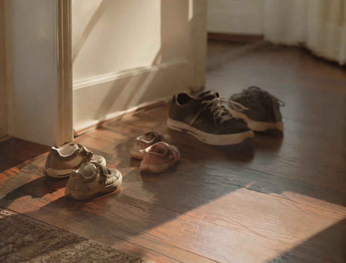 Small children's shoes and adult sneakers left in a sunlit hallway.
